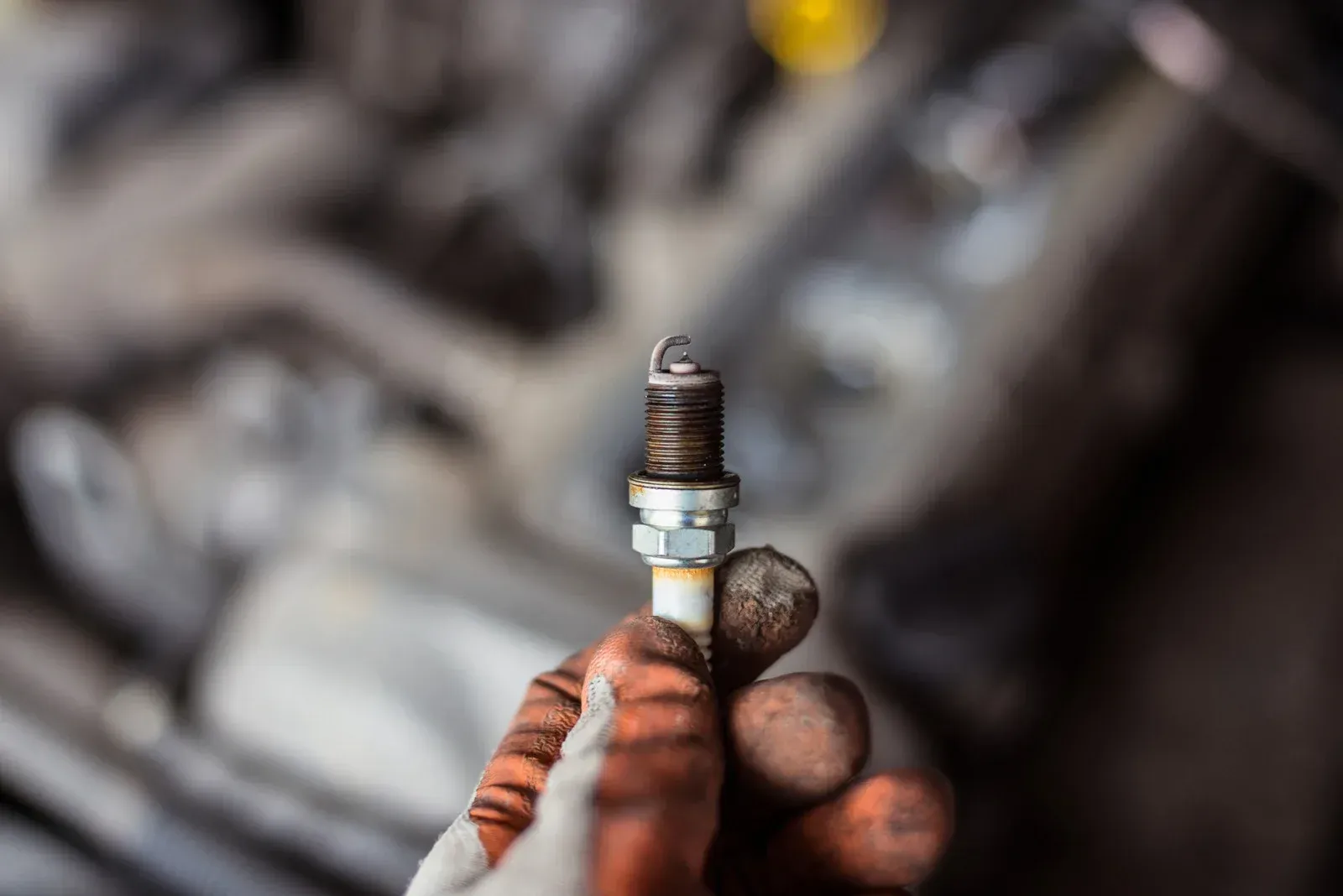 A person is holding a spark plug in their hand in front of a car engine.