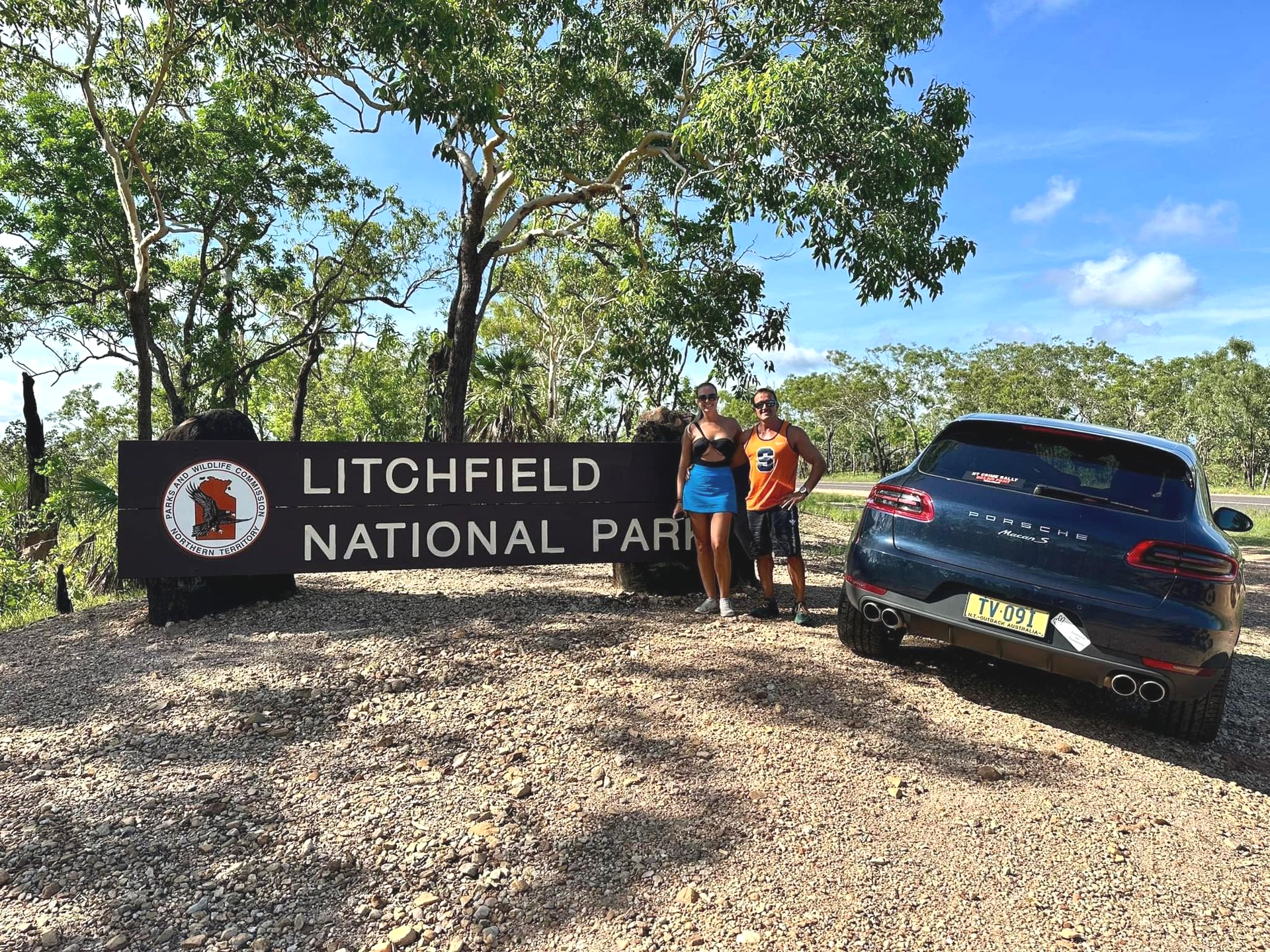 Couple stands by Litchfield National Park sign with a black car in a sunny outdoor setting — Litchfield VIP Tours In Darwin City, NT