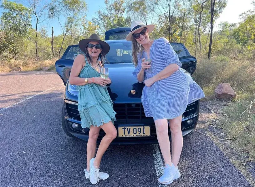 Two Women Pose With a Black Car, Holding Drinks — Litchfield VIP Tours In Darwin City, NT