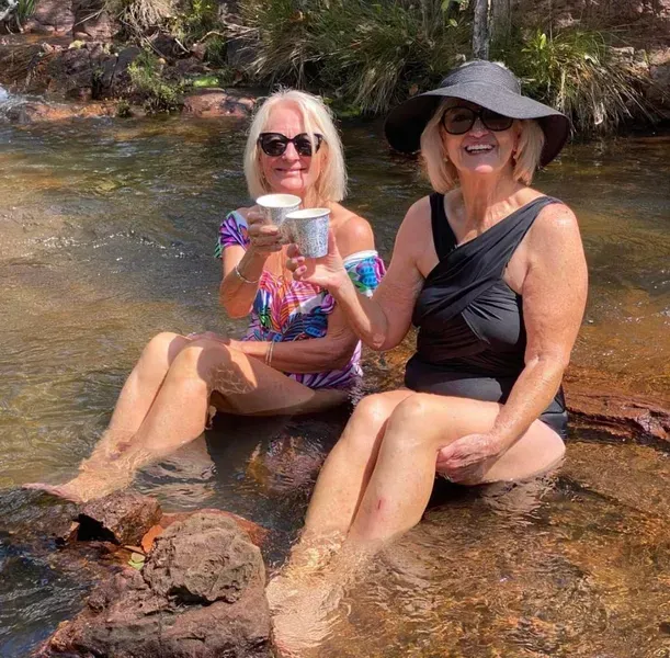 Two Women in Swimwear Sit in a Stream, Toasting With Cups — Litchfield VIP Tours In Darwin City, NT