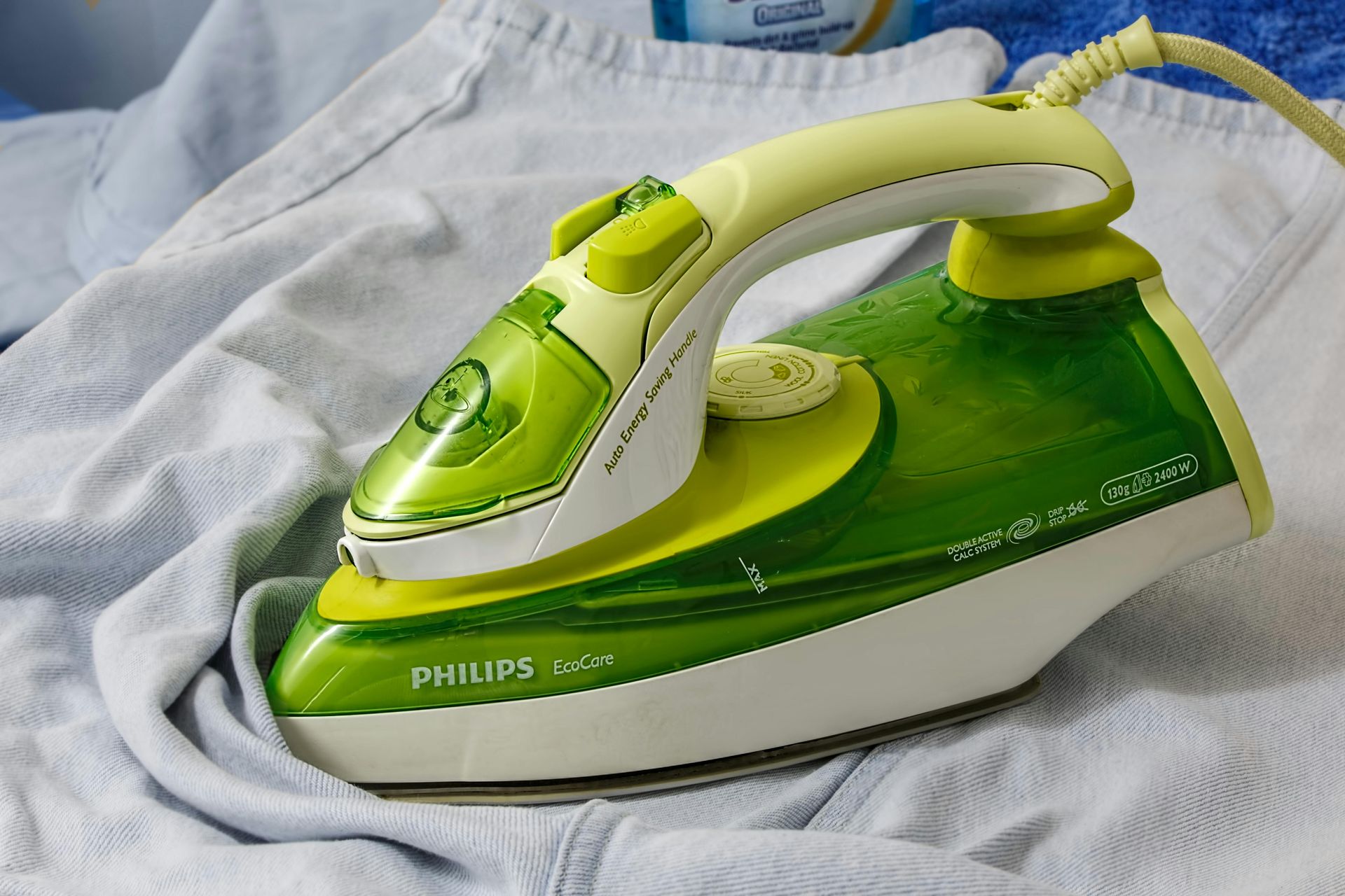 Um ferro Philips verde e branco está sobre uma camisa branca Uma mesa de madeira coberta com pratos de comida e frutas - Pousada-recanto-caxando