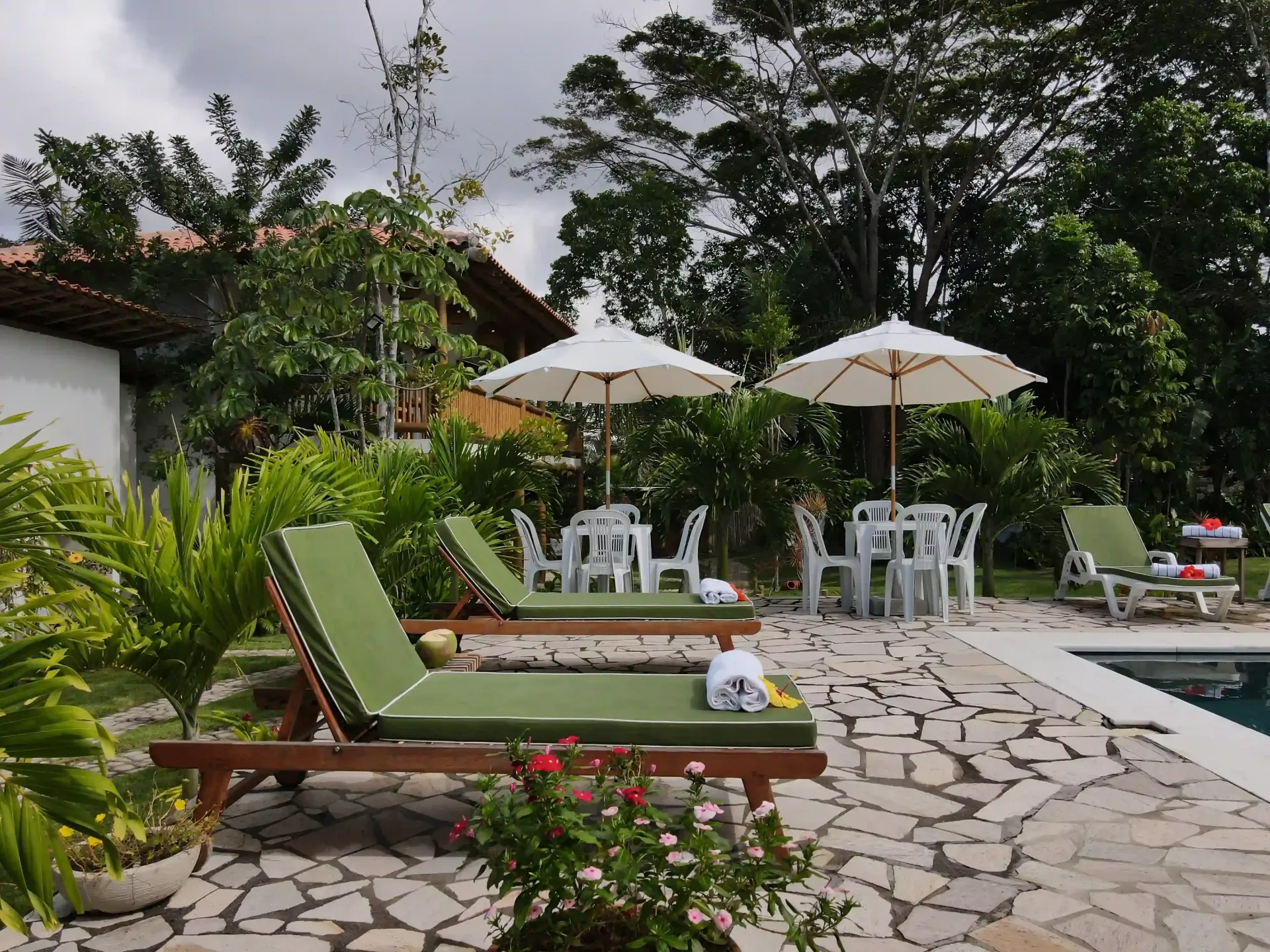 Um pátio com cadeiras e guarda-sóis ao lado de uma piscina - pousada-recanto-caxando
