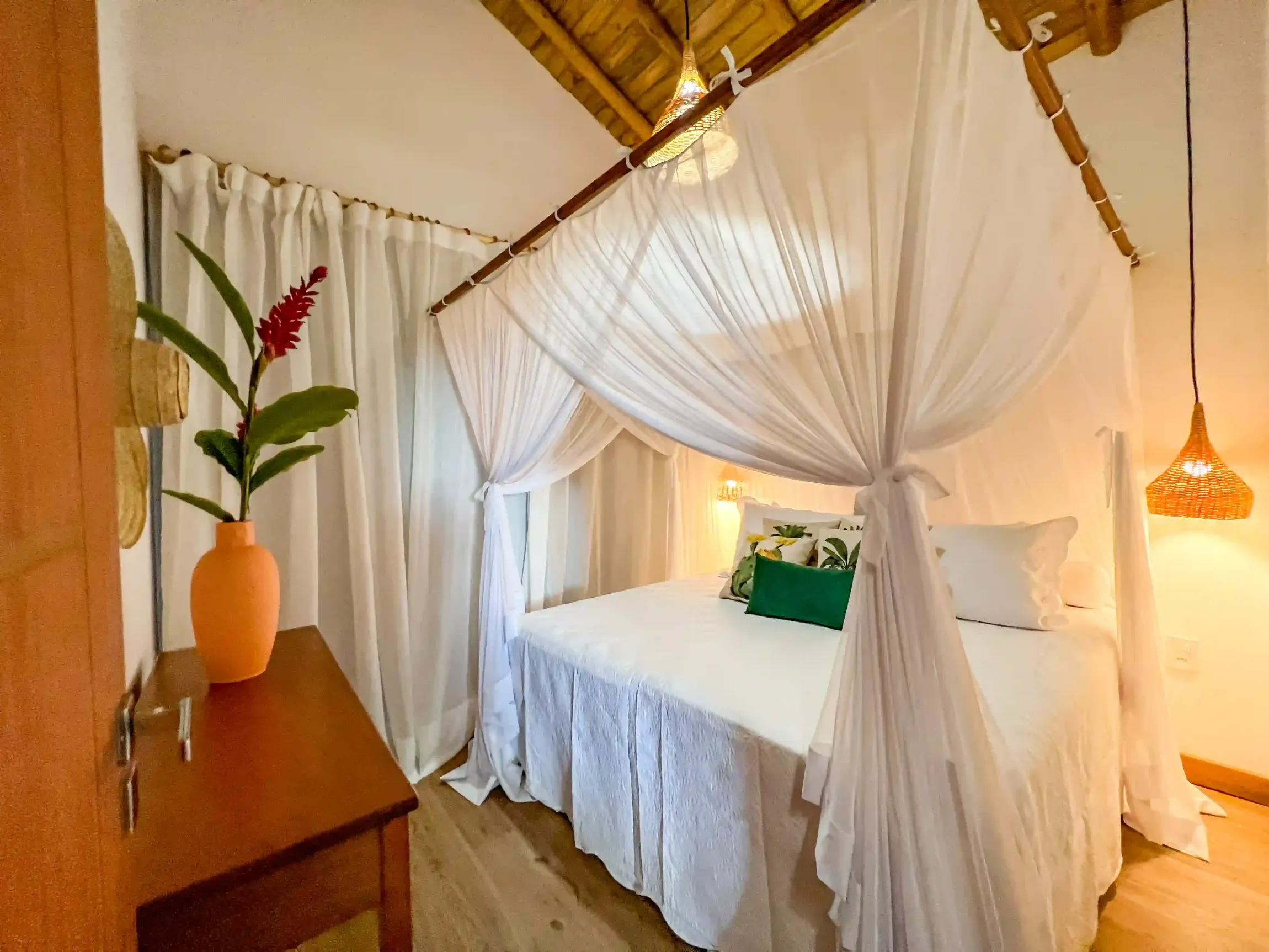 Um quarto com uma cama de dossel e um vaso de flores. pousada-recanto-caxando
