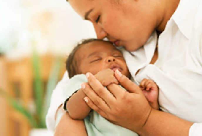 Woman kissing a baby's forehead. The baby sleeps in the woman's arms.