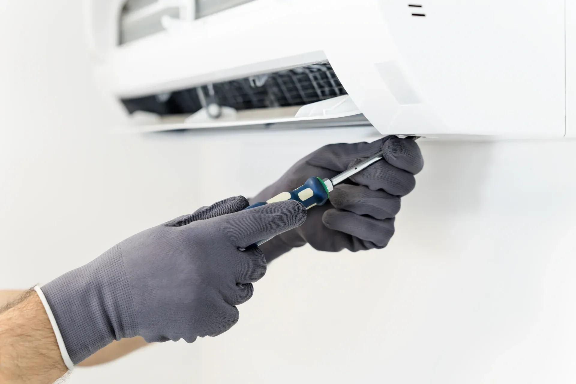 Gloved hands using a screwdriver to open the underside of a white wall-mounted air conditioner — Anthony Cameron Electrical & Solar In Woodgate, QLD