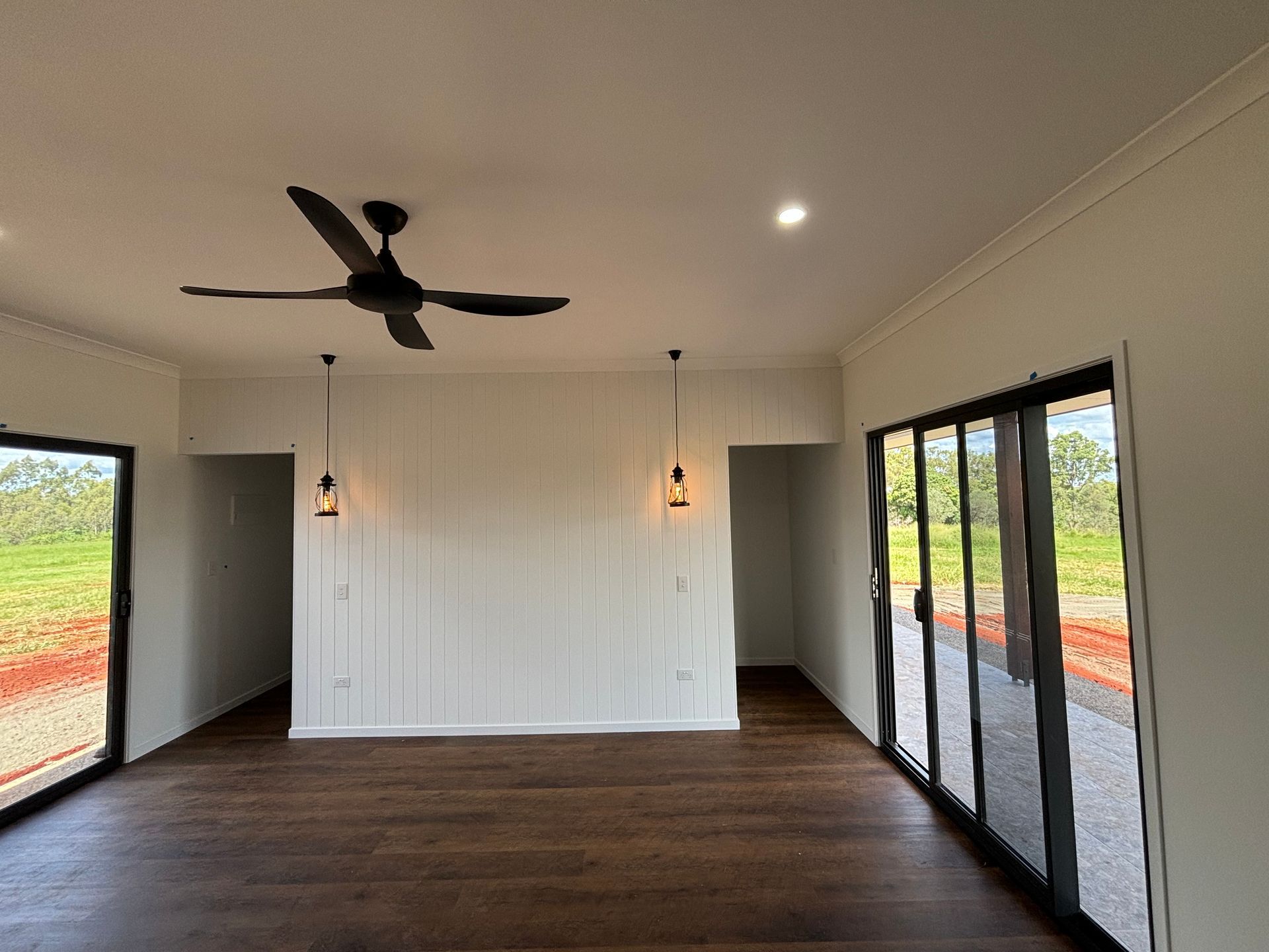 Empty modern living room with dark wood floors, ceiling fan, pendant lights, and sliding glass doors — Anthony Cameron Electrical & Solar In Kepnock, QLD