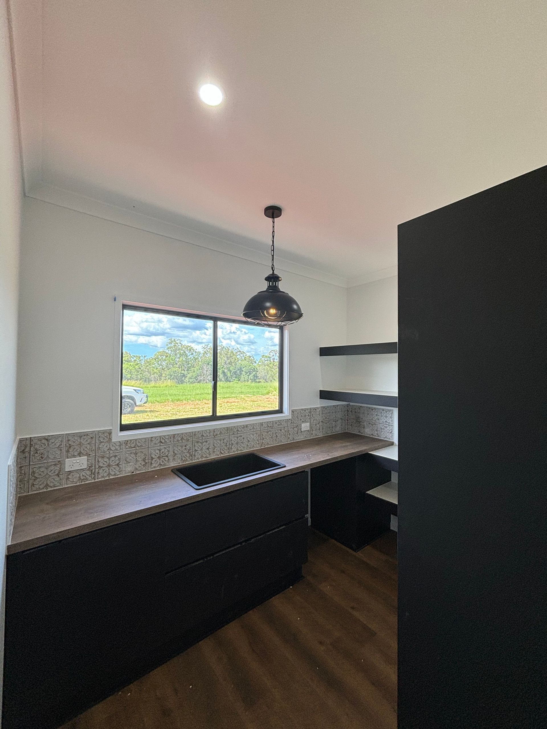 Modern kitchen with dark cabinets, granite countertops, window, and pendant light overlooking greenery — Anthony Cameron Electrical & Solar In Kepnock, QLD