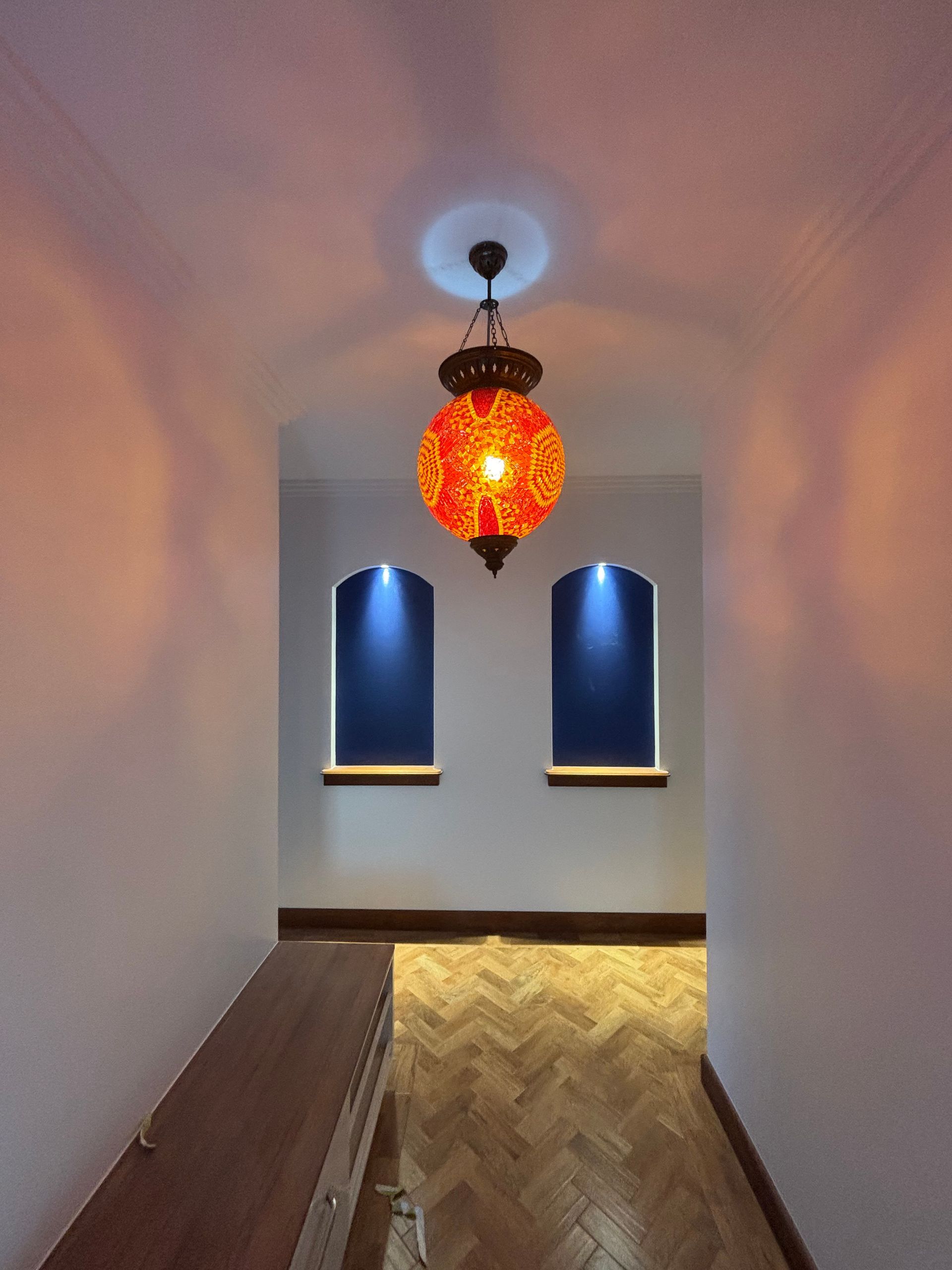 Narrow hallway with arched ceiling, hanging orange pendant light, and two blue-lit wall niches above a herringbone wood floor — Anthony Cameron Electrical & Solar In Kepnock, QLD
