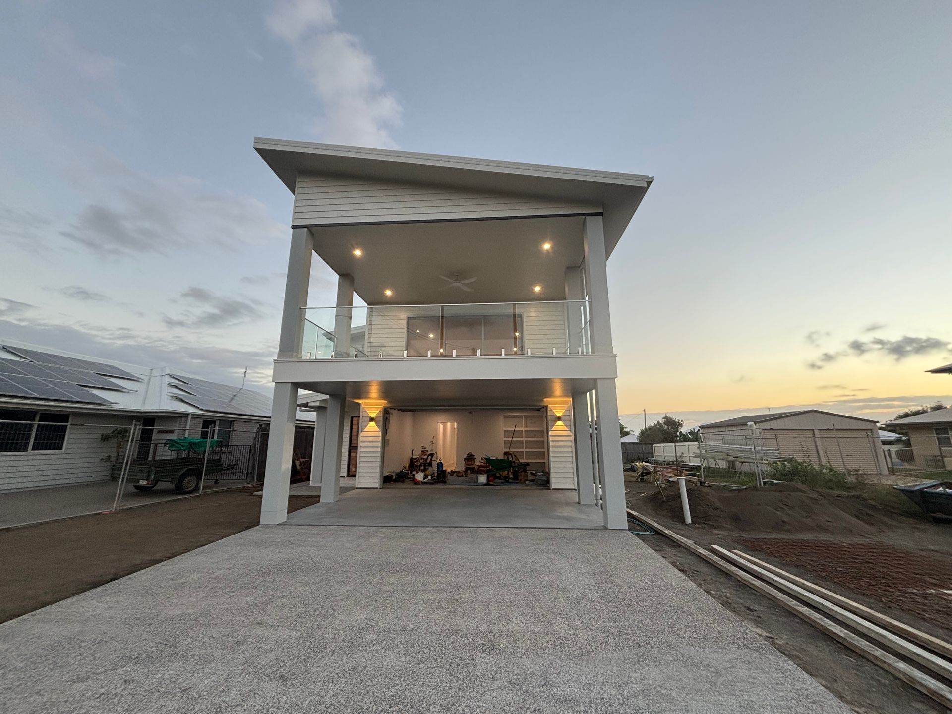 Modern two-story house with a lit balcony and wide gravel driveway at dusk — Anthony Cameron Electrical & Solar In Kepnock, QLD