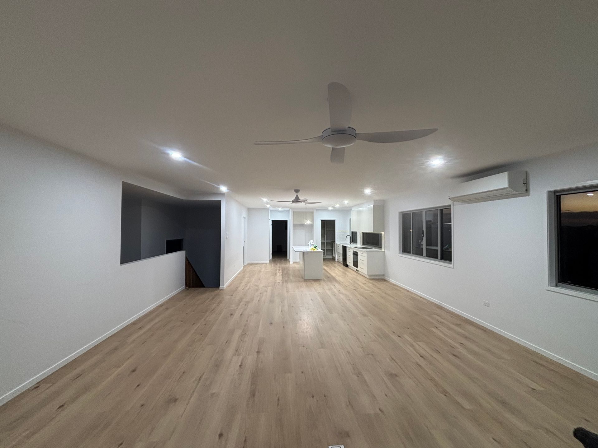 Spacious empty modern living room with wood floors, white walls, ceiling fan, and kitchen at the far end — Anthony Cameron Electrical & Solar In Kepnock, QLD