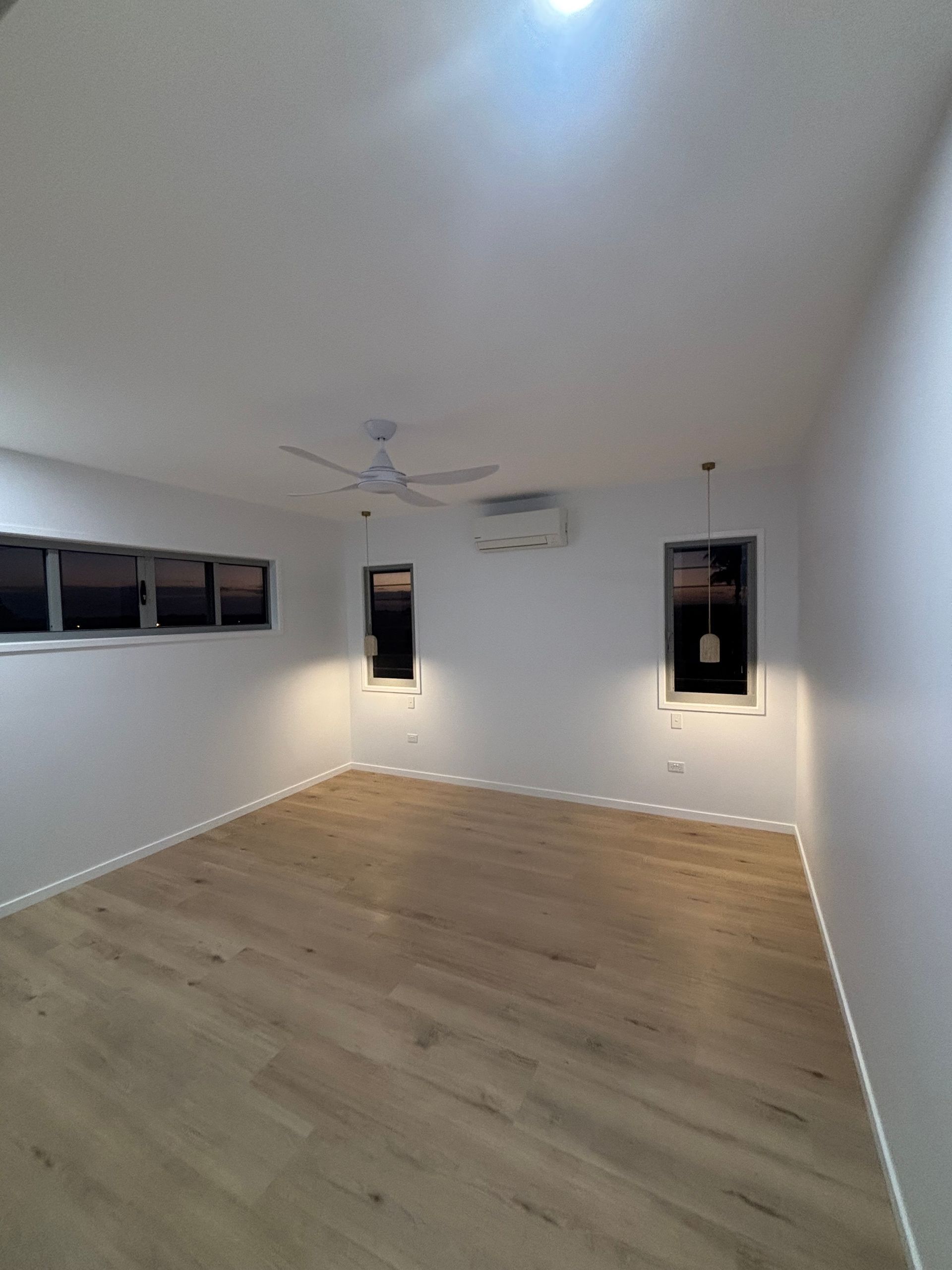 Empty white room with light wood floor, ceiling fan, and small black-framed windows — Anthony Cameron Electrical & Solar In Kepnock, QLD