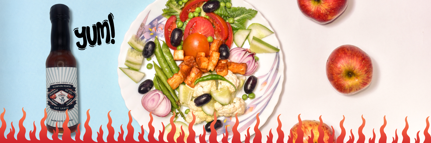 A bottle of hot sauce next to a plate of salad and apples.