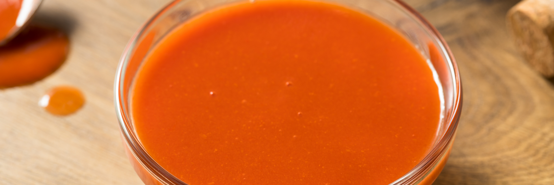 A close up of a container of hot sauce on a wooden table. A close up of a container of hot sauce on a wooden table.