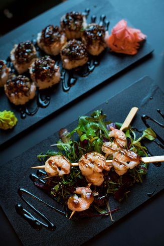 There are two plates of food on the table , one of which is a salad with shrimp on skewers.