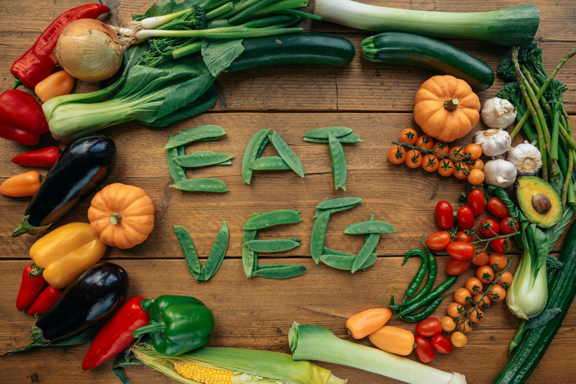 A wooden table topped with vegetables and the words `` eat veg '' written in green letters. A wooden table topped with vegetables and the words `` eat veg '' written in green letters.