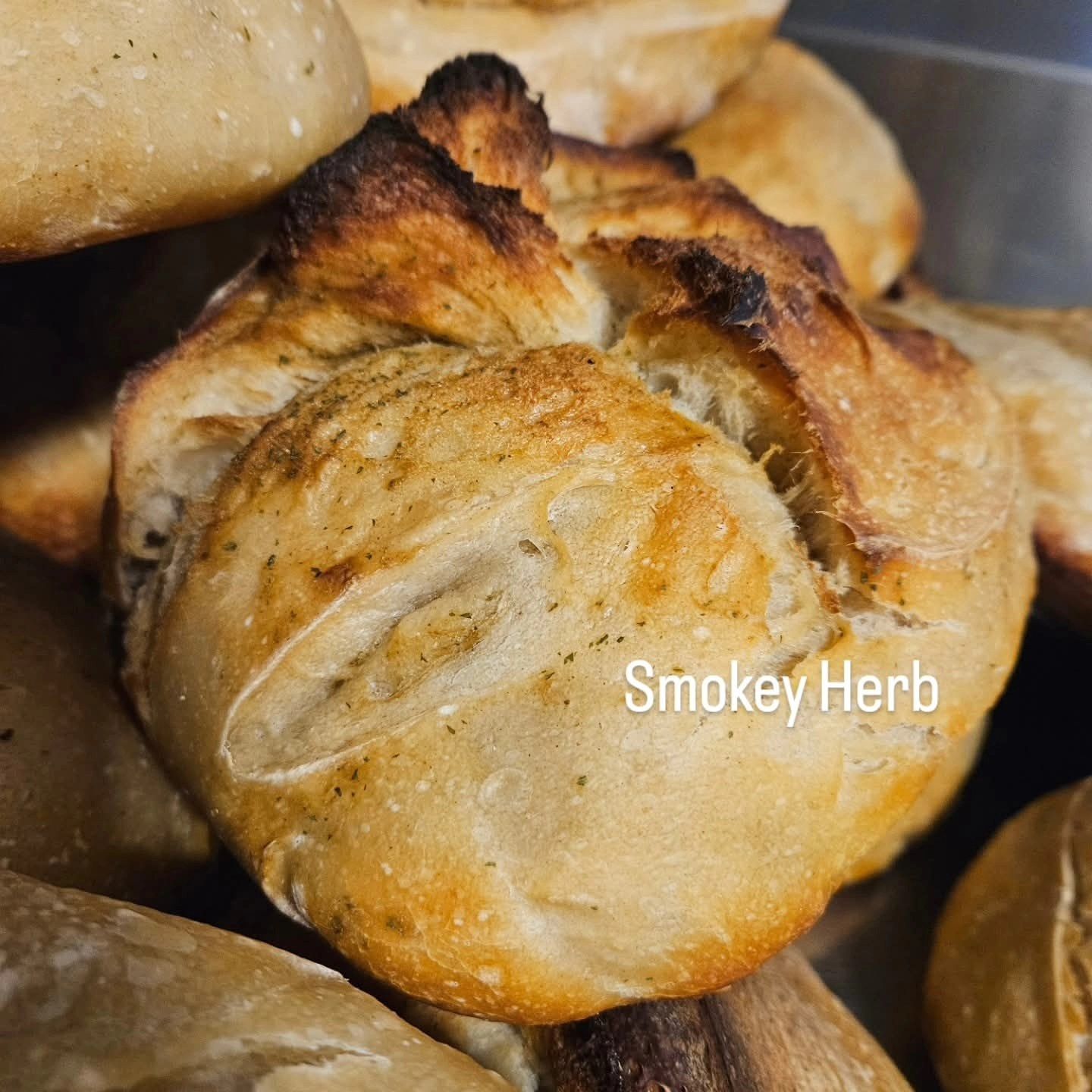 A golden-brown, rustic-style artisan bread roll with herbs, labeled A golden-brown, rustic-style artisan bread roll with herbs, labeled