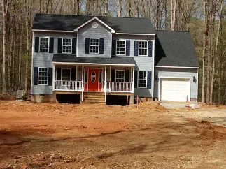 Two-story house with gray siding, black roof, and red front door. White trim and blue shutters, next to a garage.