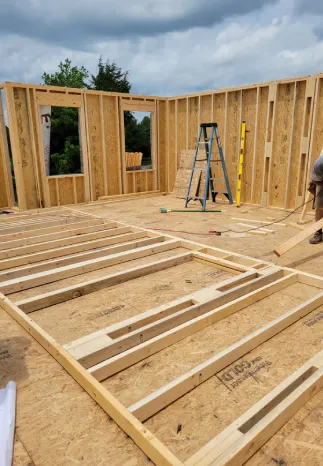 Interior framing of a house under construction; wood studs, windows, and a ladder are visible.