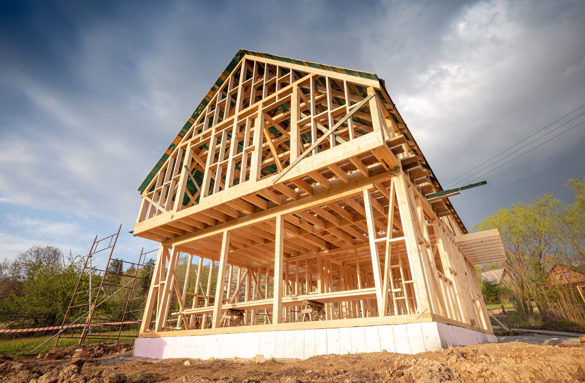 Wooden house frame under construction, set against a cloudy sky.