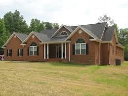 A one-story brick house with a dark gabled roof, white columns at the entrance, and arched windows on a grassy lot.