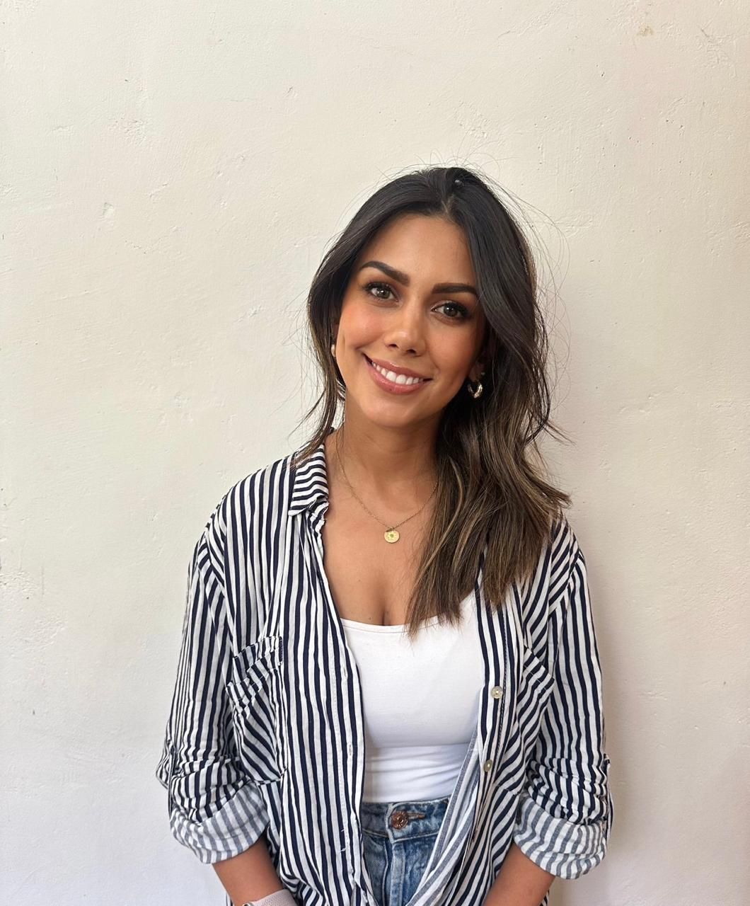 A woman wearing a striped shirt and a white tank top is smiling.