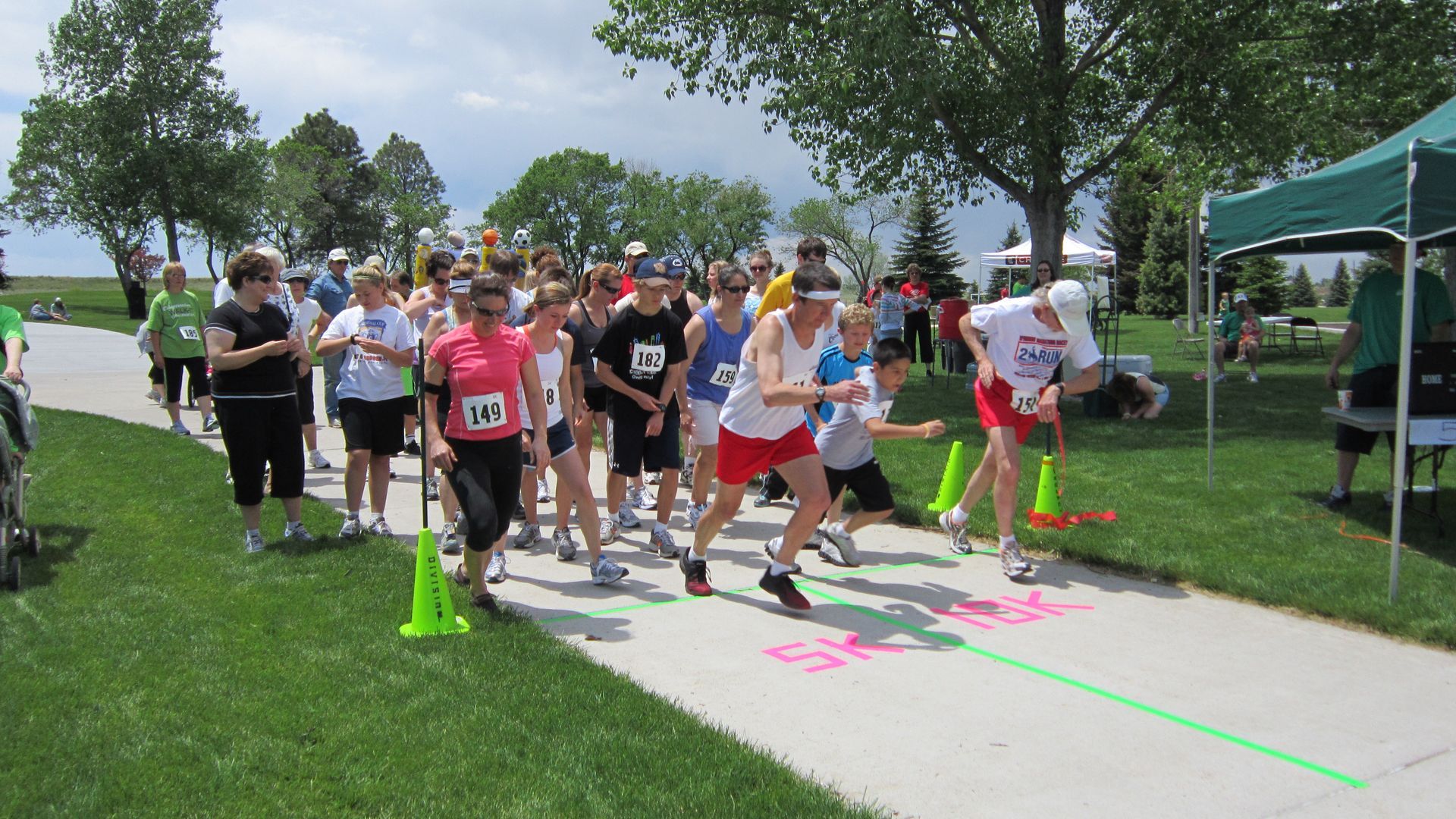 Runners at the starting line of a 5k race, outdoor setting with spectators and green grass.