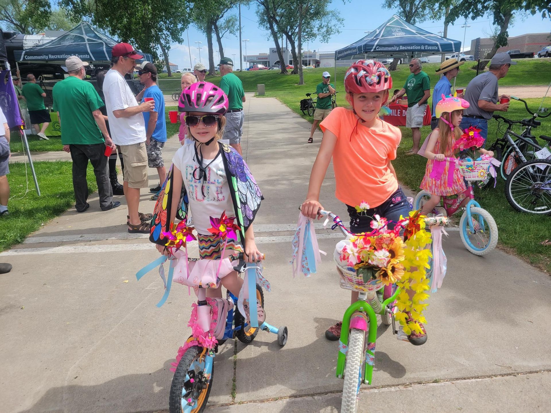 Two young girls on decorated bikes posing outdoors, wearing helmets.