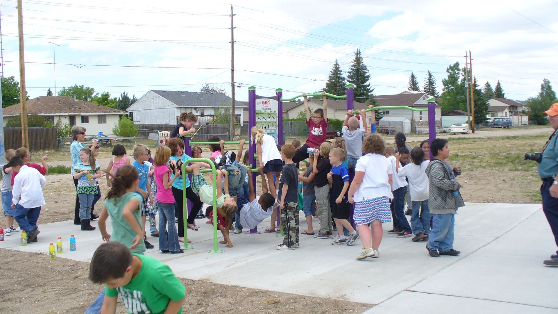 Children on playground equipment, some hanging, others watching. Outdoors on a sunny day.