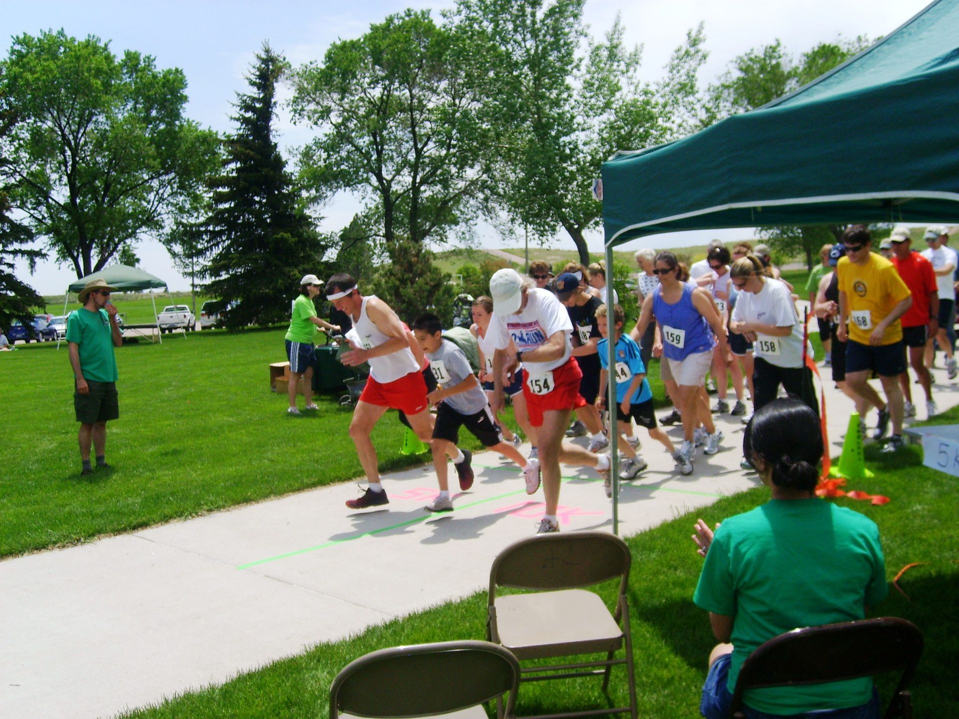 People running at the start of a race on a paved path, under a tent in a park.