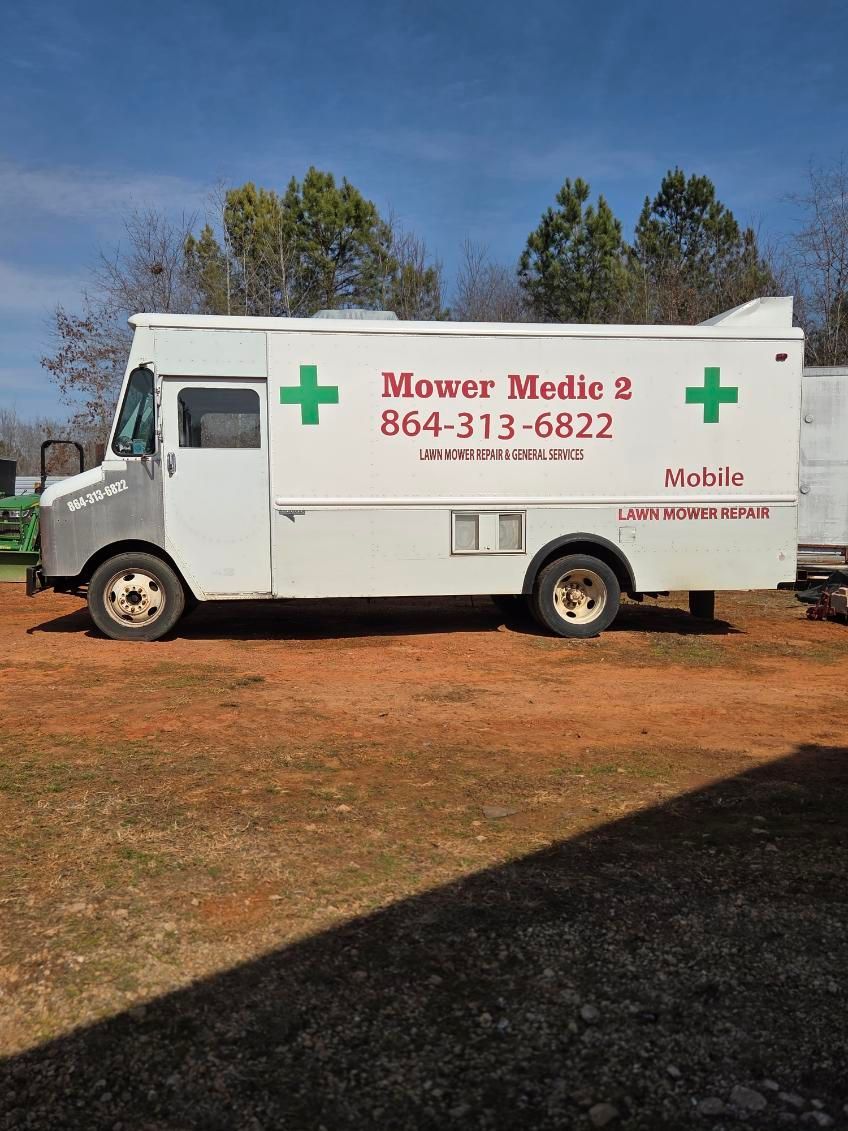 White mobile medical truck with red cross and “Mawar Medina” parked on a dirt lot under a blue sky.