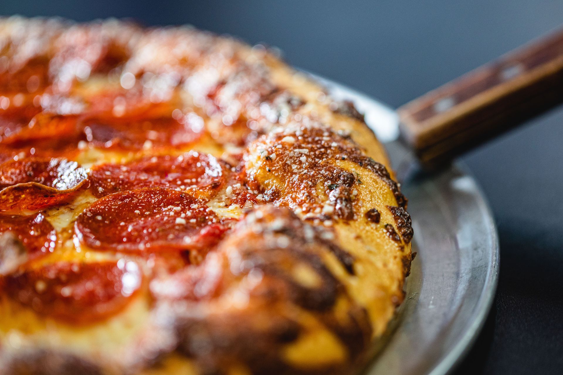 Close-up of a pepperoni pizza with parmesan-topped crust on a metal pan