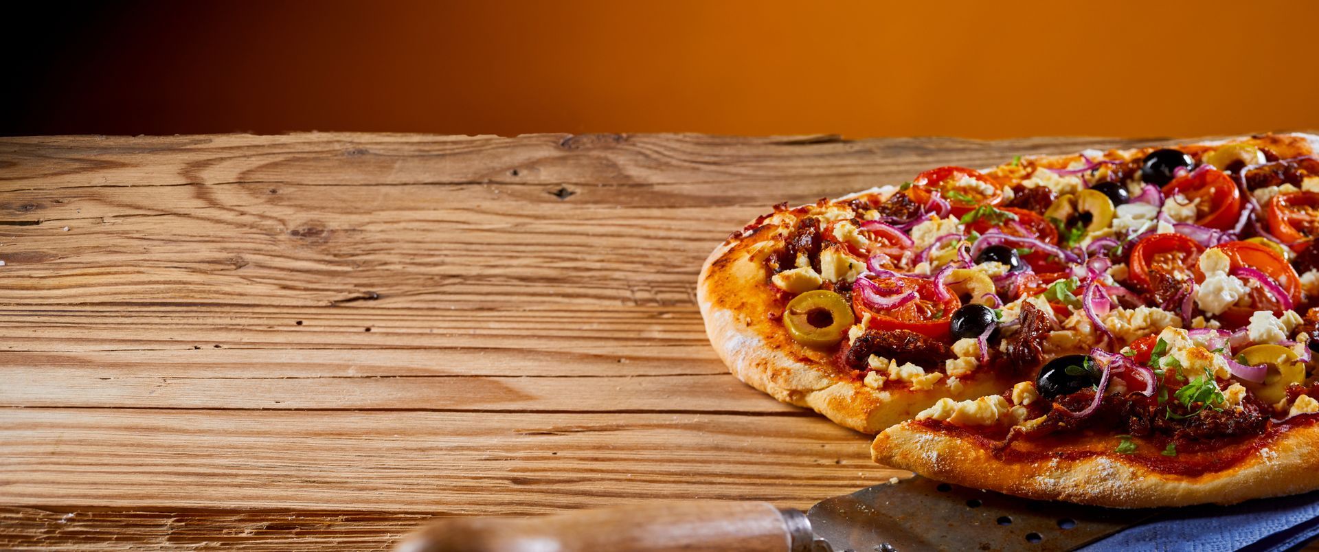 Greek-style customized pizzas on a rustic wooden table topped with olives, feta, and fresh onions.