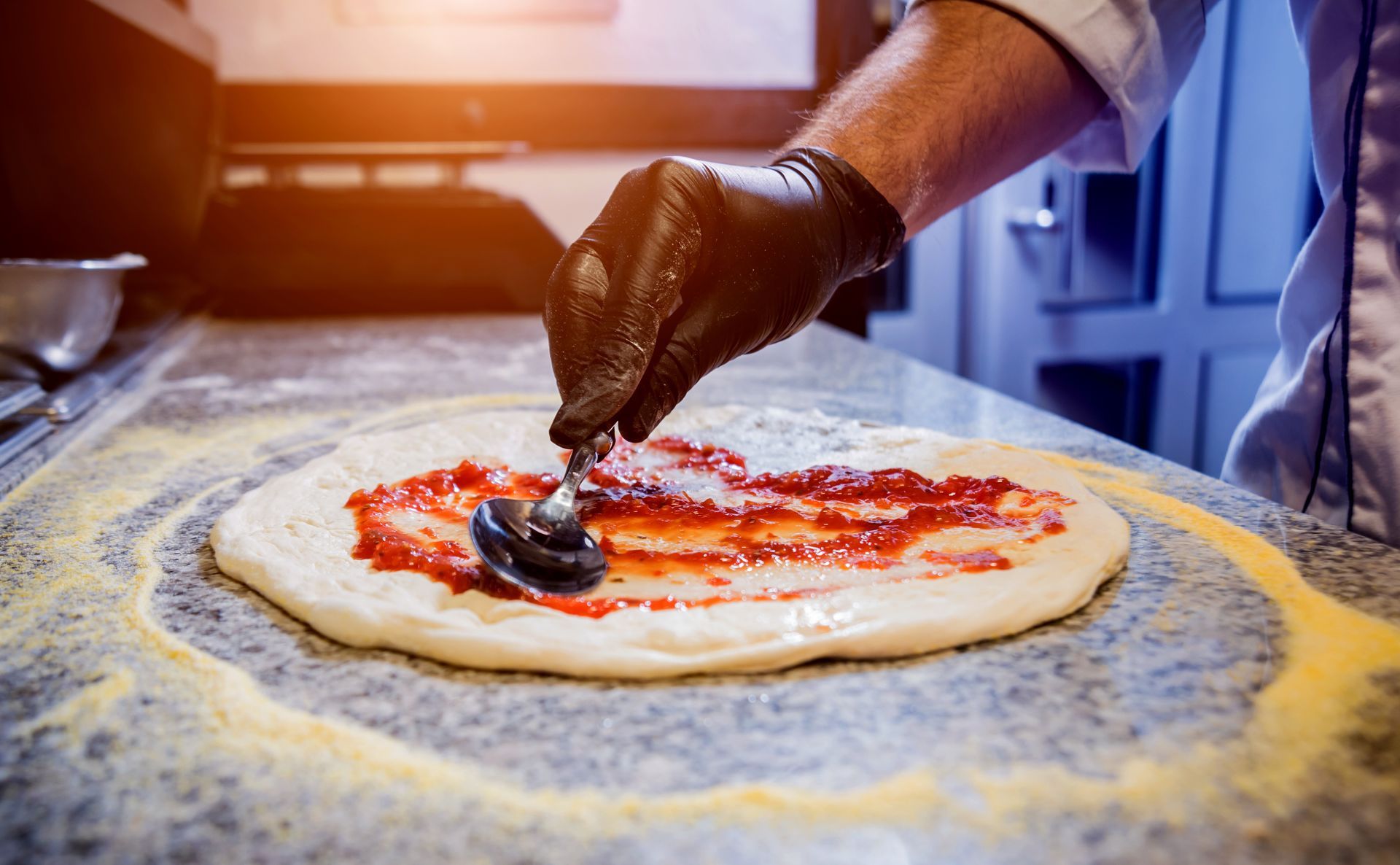 Chef spreading tomato sauce on pizza dough during custom pizza preparation. Chef spreading tomato sauce on pizza dough during custom pizza preparation.