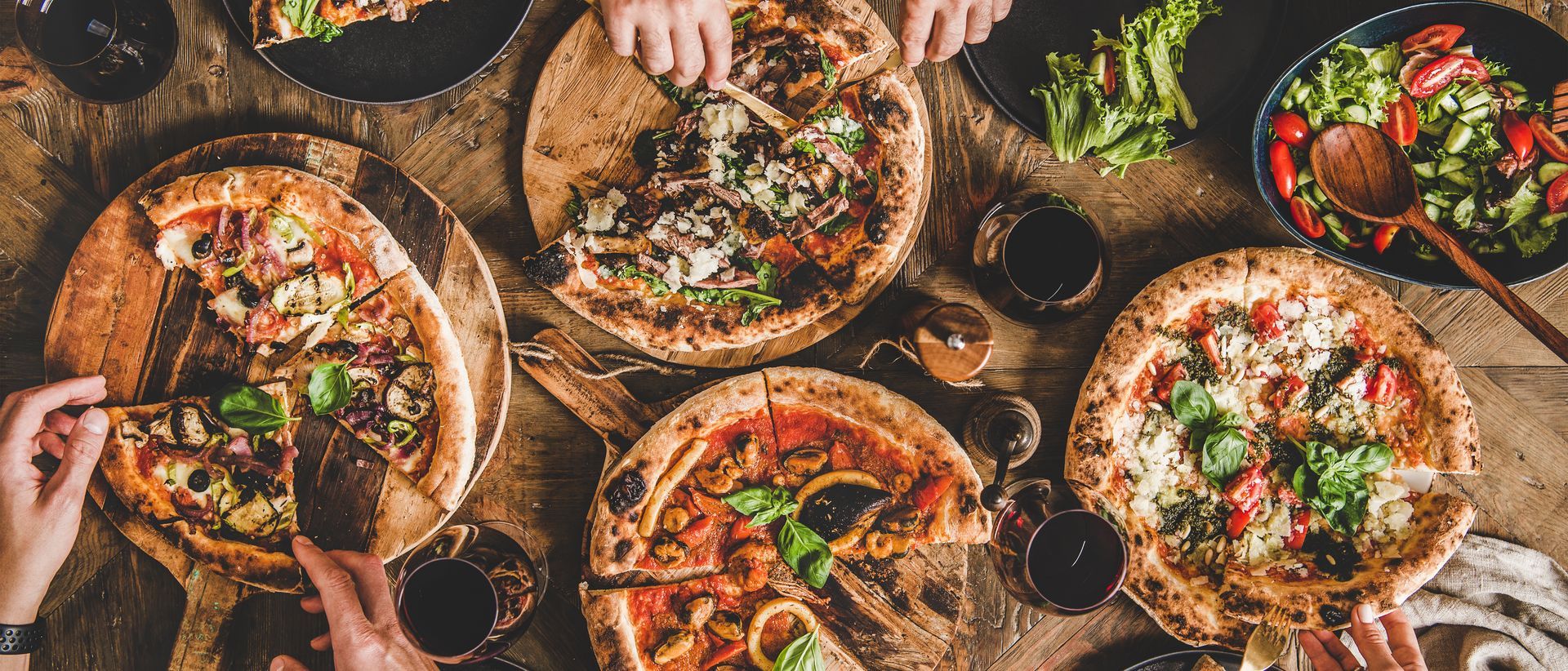 Assorted pizzas, fresh salad, and drinks served on a rustic table during a shared meal.