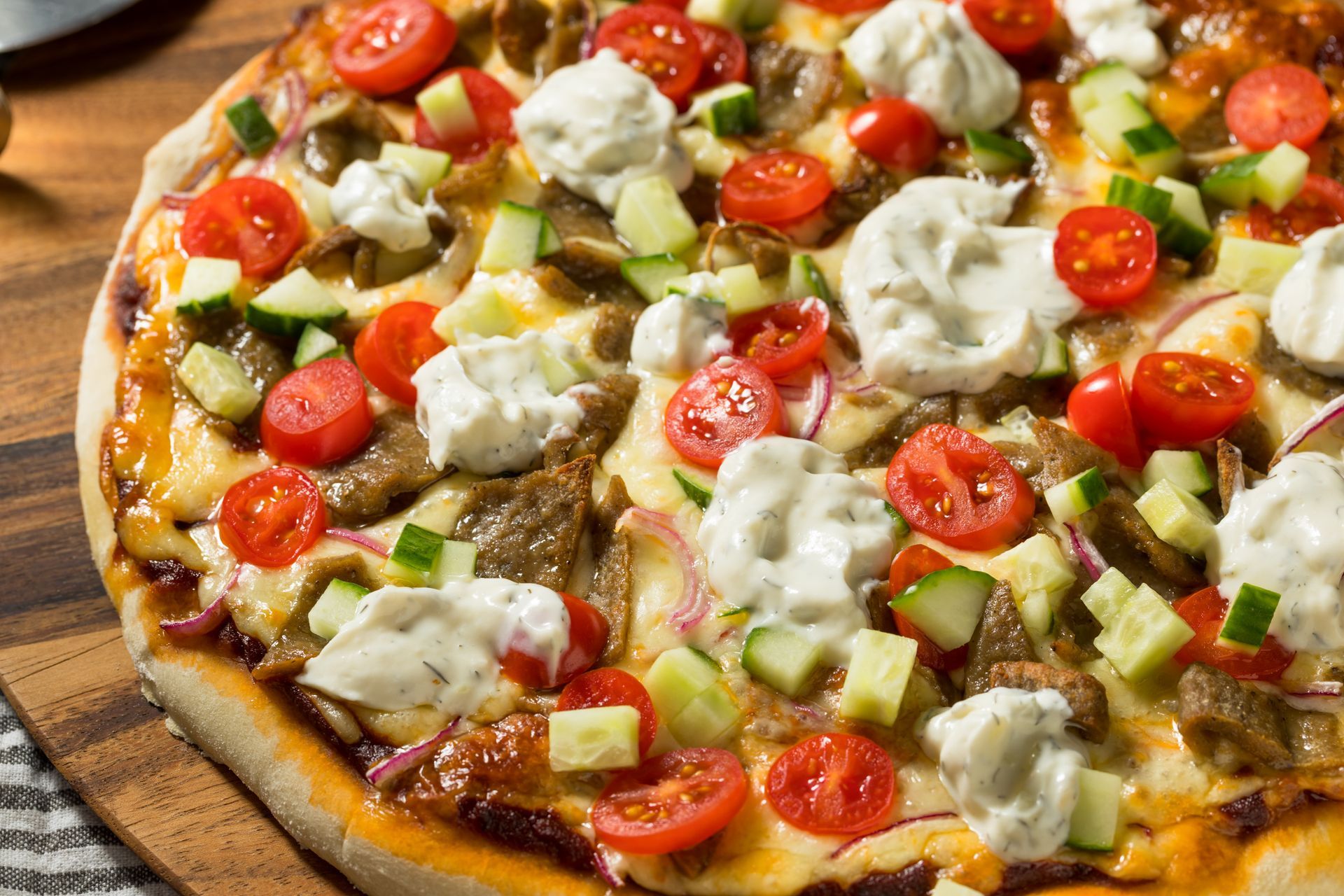 A specialty Greek gyro pizza with tzatziki sauce and tomatoes from a pizza restaurant. A specialty Greek gyro pizza with tzatziki sauce and tomatoes from a pizza restaurant.