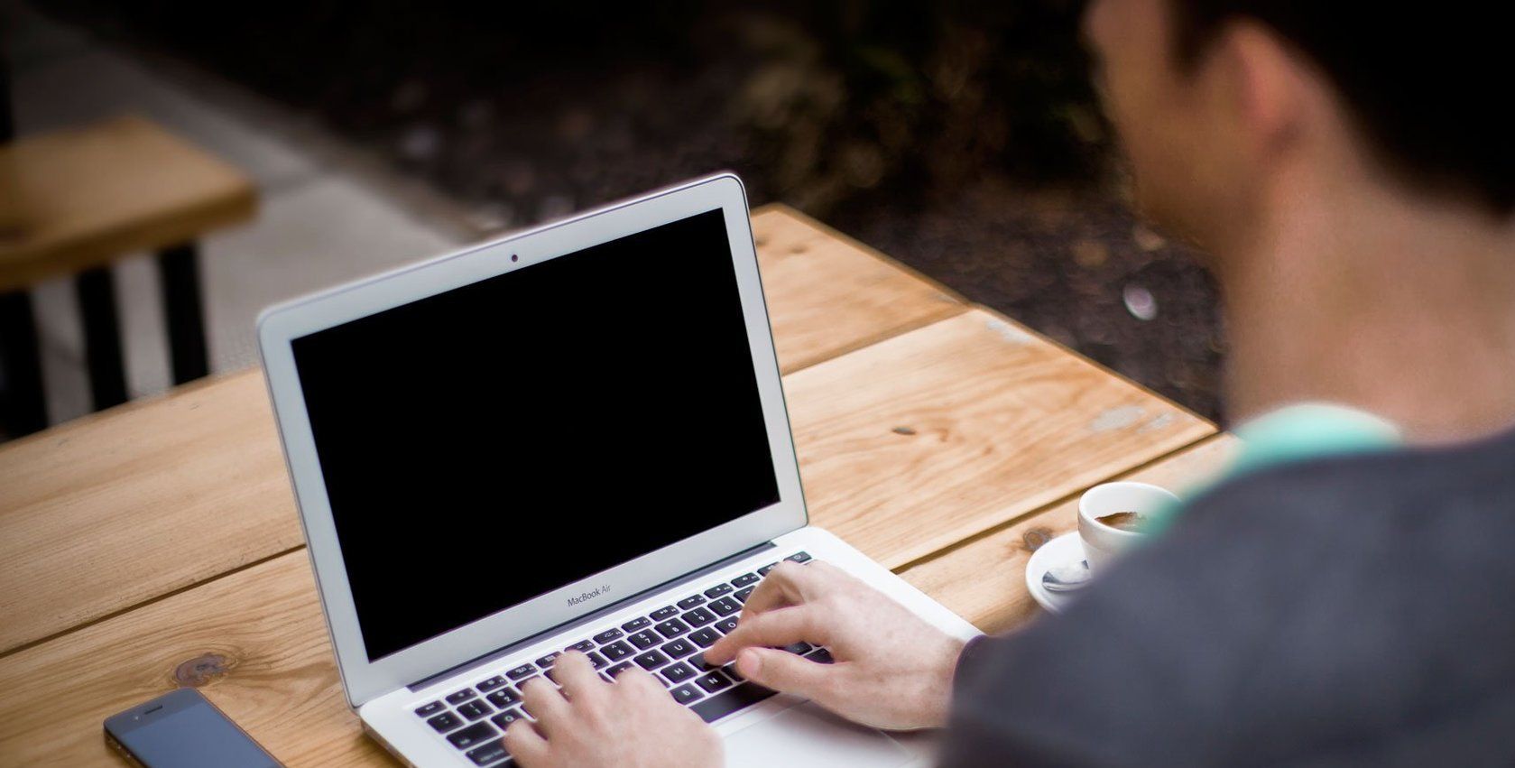 A man is typing on a laptop computer at a wooden table.