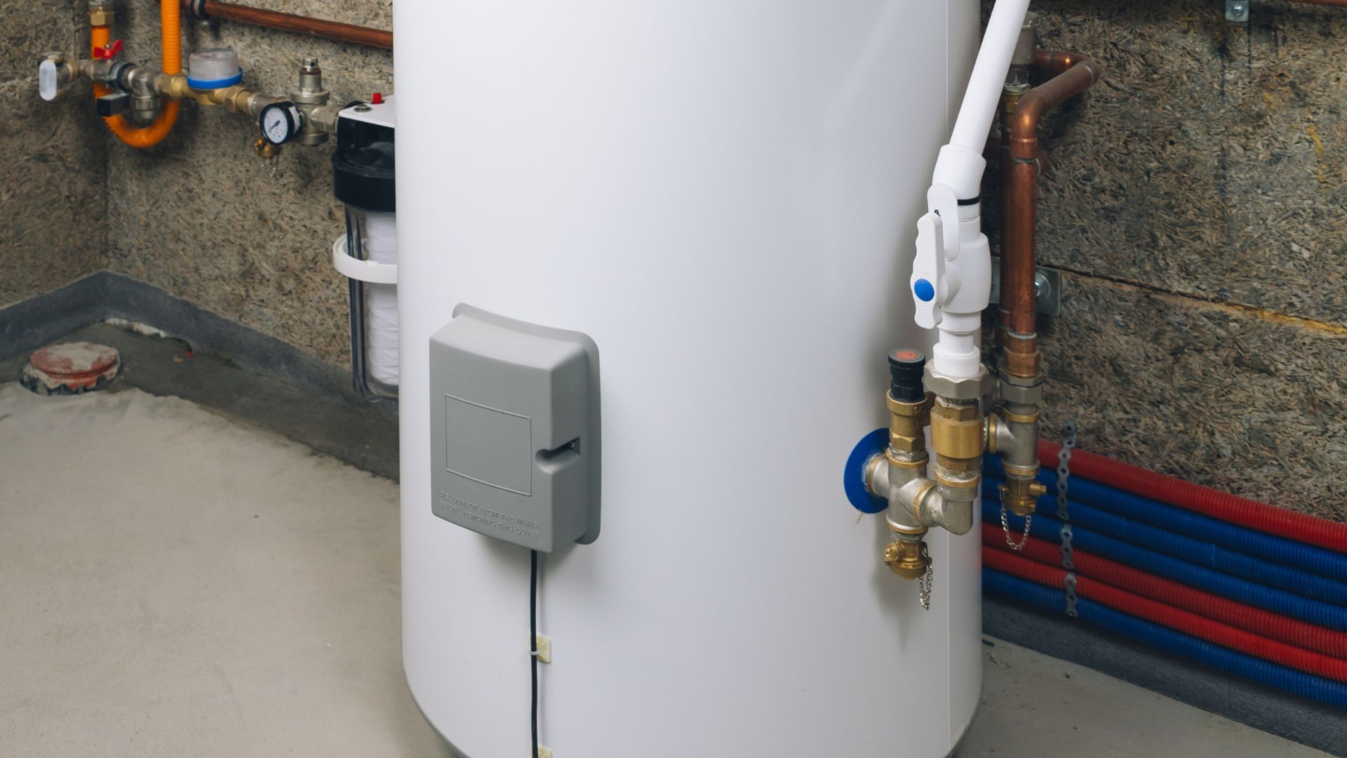 A white water heater is sitting in a room with pipes.