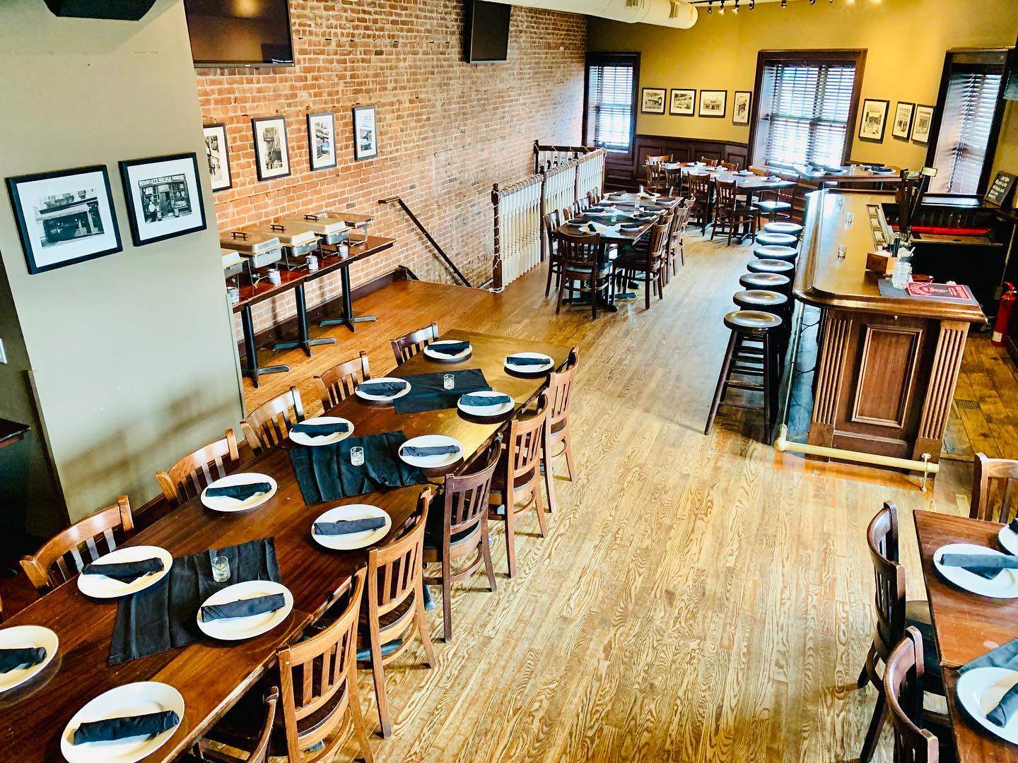 A high-angle view of a restaurant interior featuring rows of tables with place settings, brick walls, and a wooden bar.