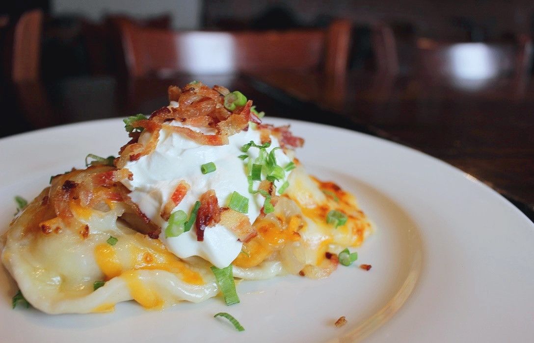 A plate of cheesy pierogis topped with sour cream, bacon bits, and chopped green onions.
