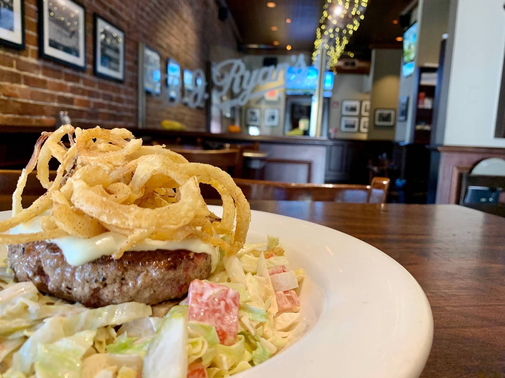 A burger patty topped with crispy fried onions on a bed of salad in a restaurant with brick walls and hanging lights.