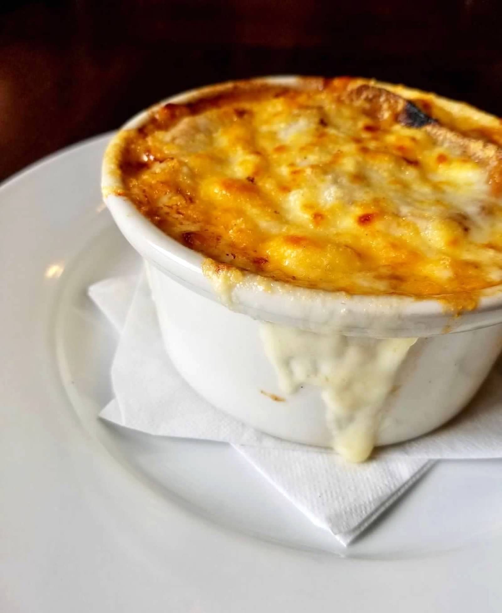 A white ceramic ramekin of baked, bubbly macaroni and cheese with melted, browned cheese on a white plate.