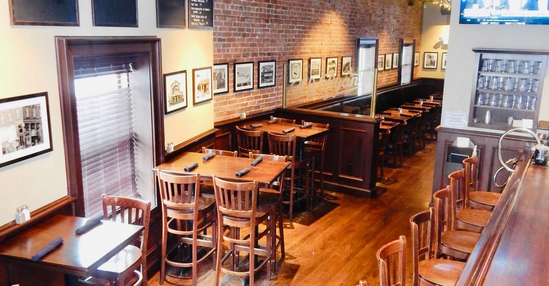 An elevated view of a restaurant interior featuring wooden tables, chairs, bar seating, and framed pictures on brick walls.