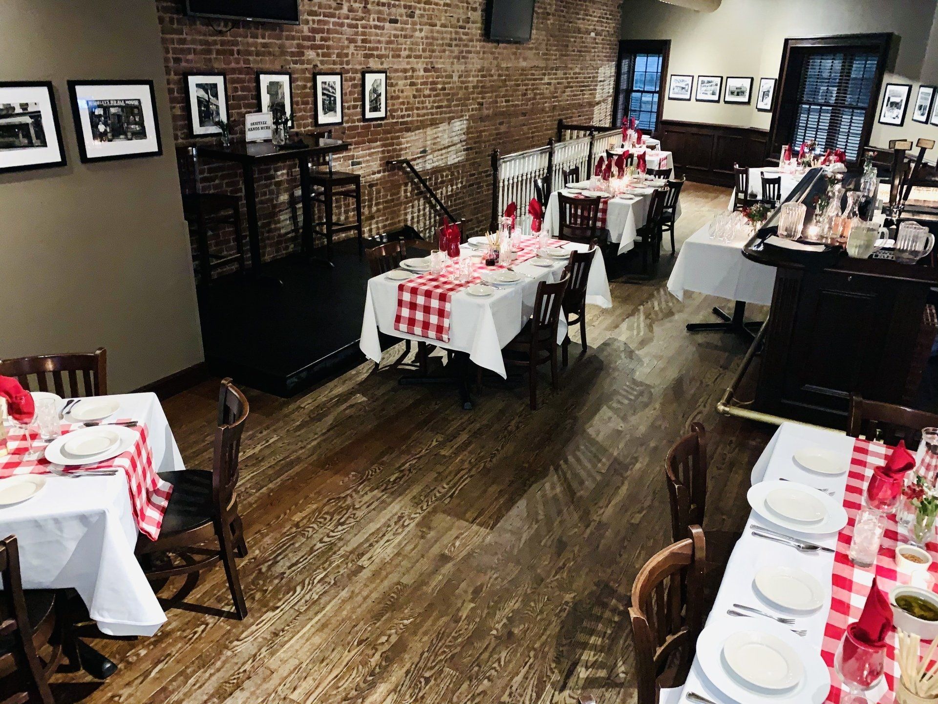 High-angle shot of a restaurant dining room featuring wood floors, exposed brick walls, and tables set with checkered cloths.