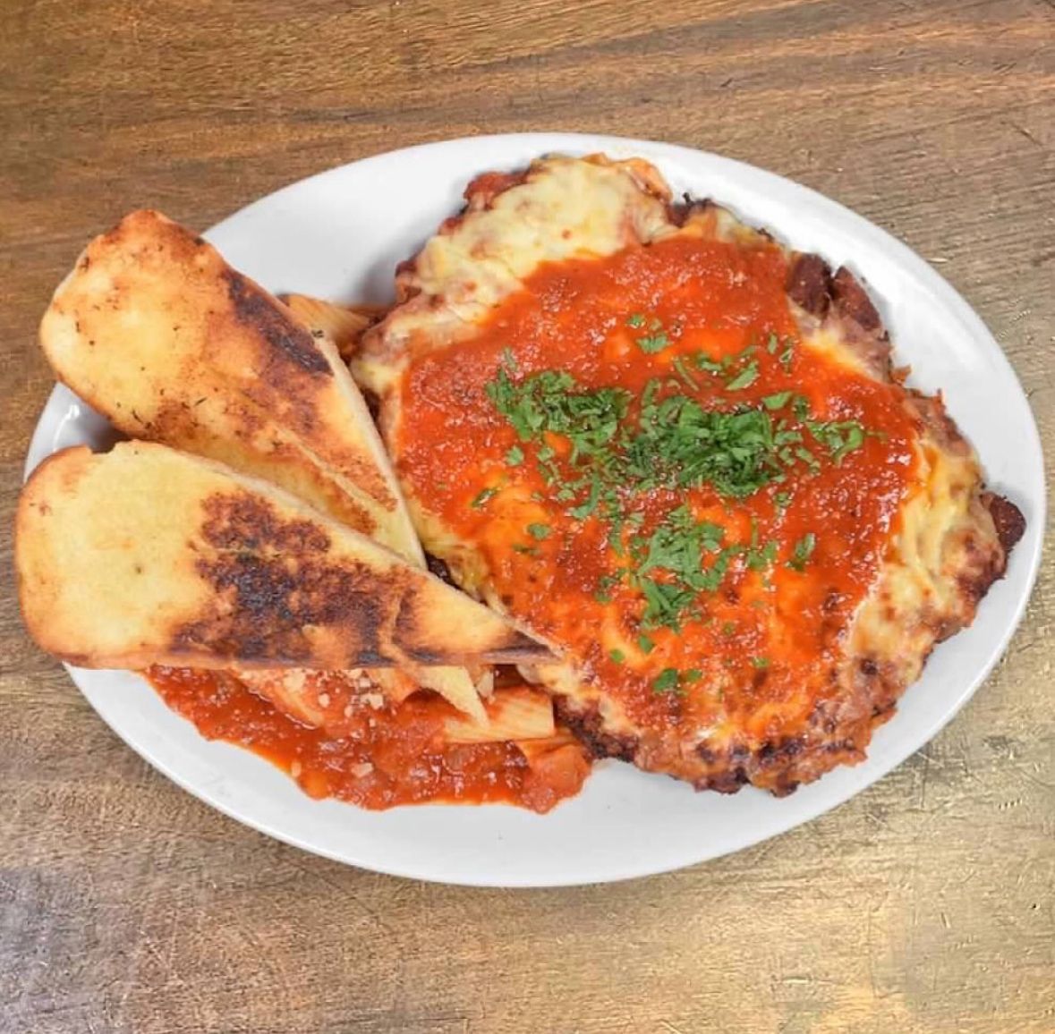 A plate of chicken parmesan topped with melted cheese, marinara sauce, and herbs, served with two pieces of toasted bread.