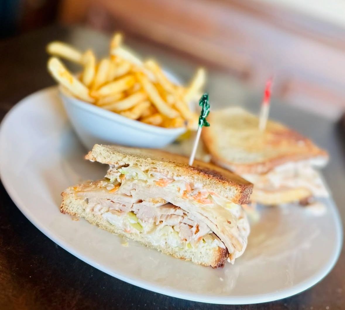 A toasted turkey sandwich with coleslaw and a side of french fries on a white plate.