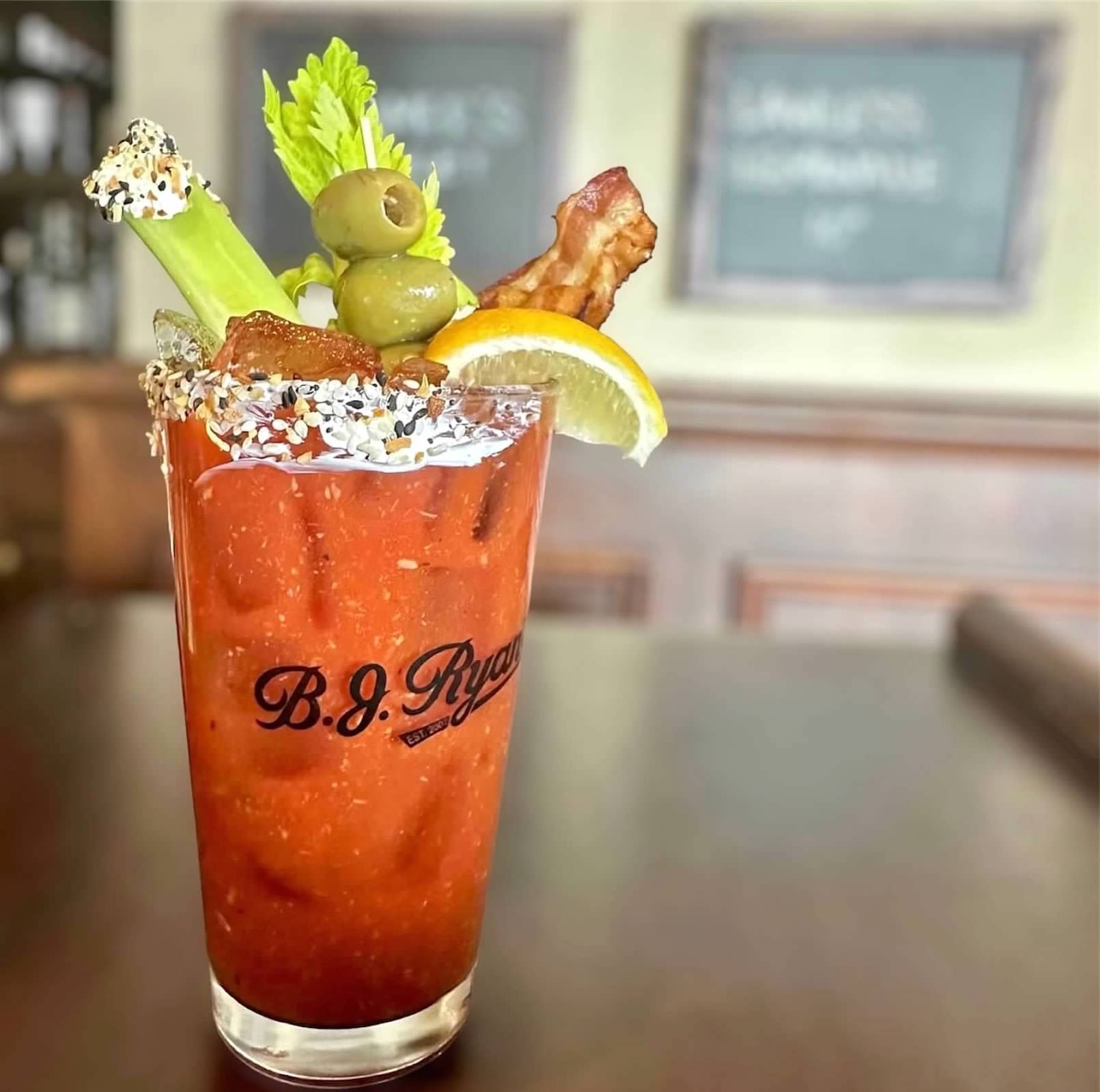 A B.J. Ryan’s bloody mary cocktail garnished with a celery stalk, olives, bacon, and a lemon wedge in a seasoned glass.