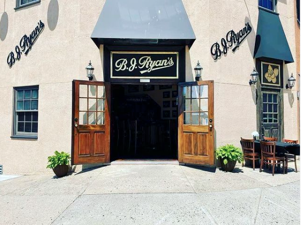 The exterior of B.J. Ryan’s restaurant, featuring a double wooden door entrance, awnings, and outdoor seating.