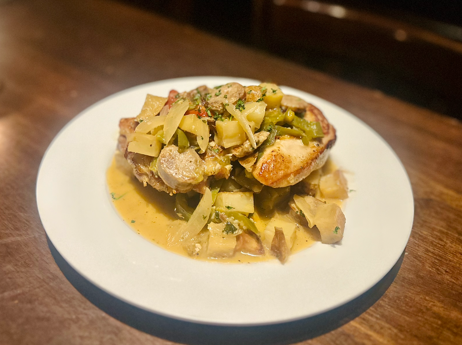 A plated dish of sautéed chicken topped with artichokes and peppers in a creamy sauce, set on a dark wooden table.