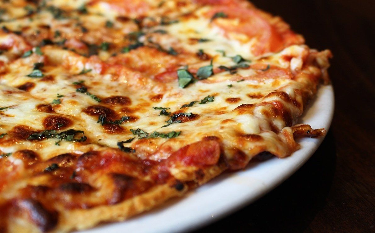 A close-up of a thin-crust pizza topped with melted cheese, tomato sauce, and fresh basil, served on a white plate.