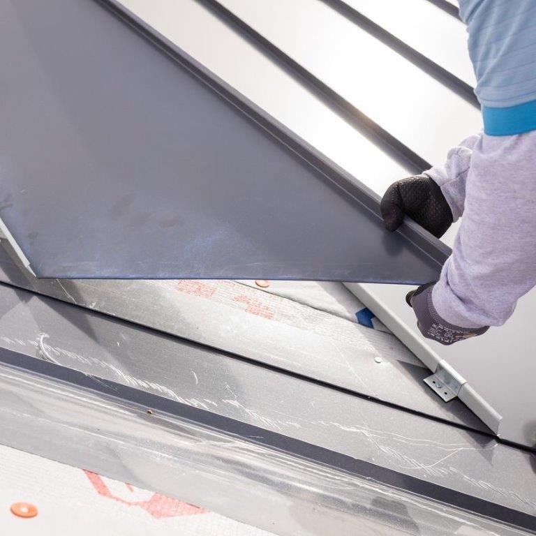 Person installing a dark metal roof panel on a building.